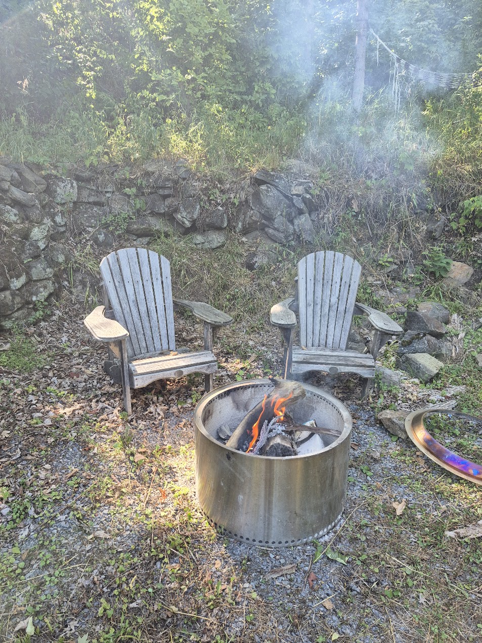 Campfire area with Adirondack chairs and stone backdrop, overlooking the marsh